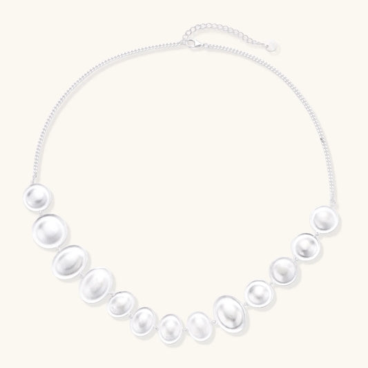 Graduated pearl-finish silver discs forming an organic bubble bib necklace on delicate chain against cream background.