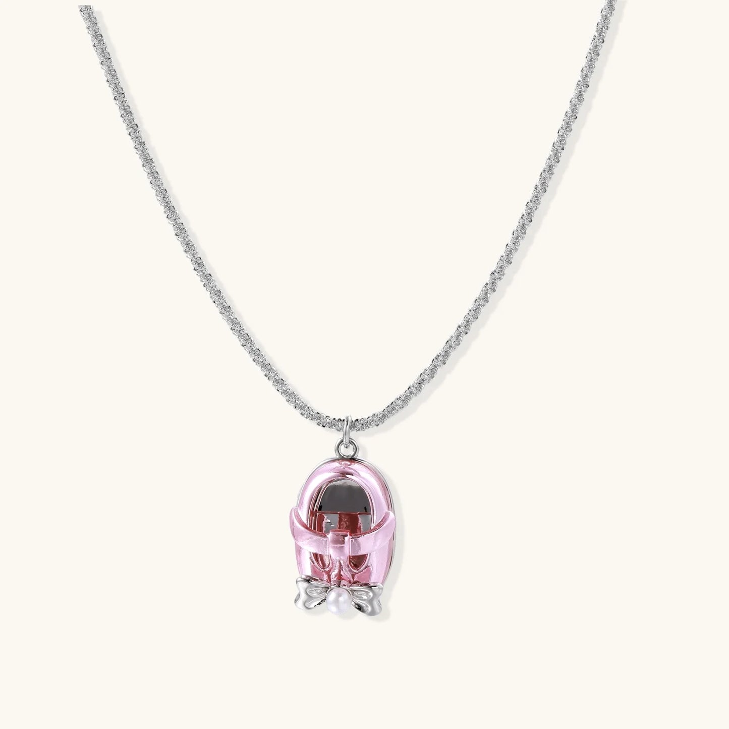 Translucent pink skull pendant with silver bow detail on delicate white gold plated chain against cream background