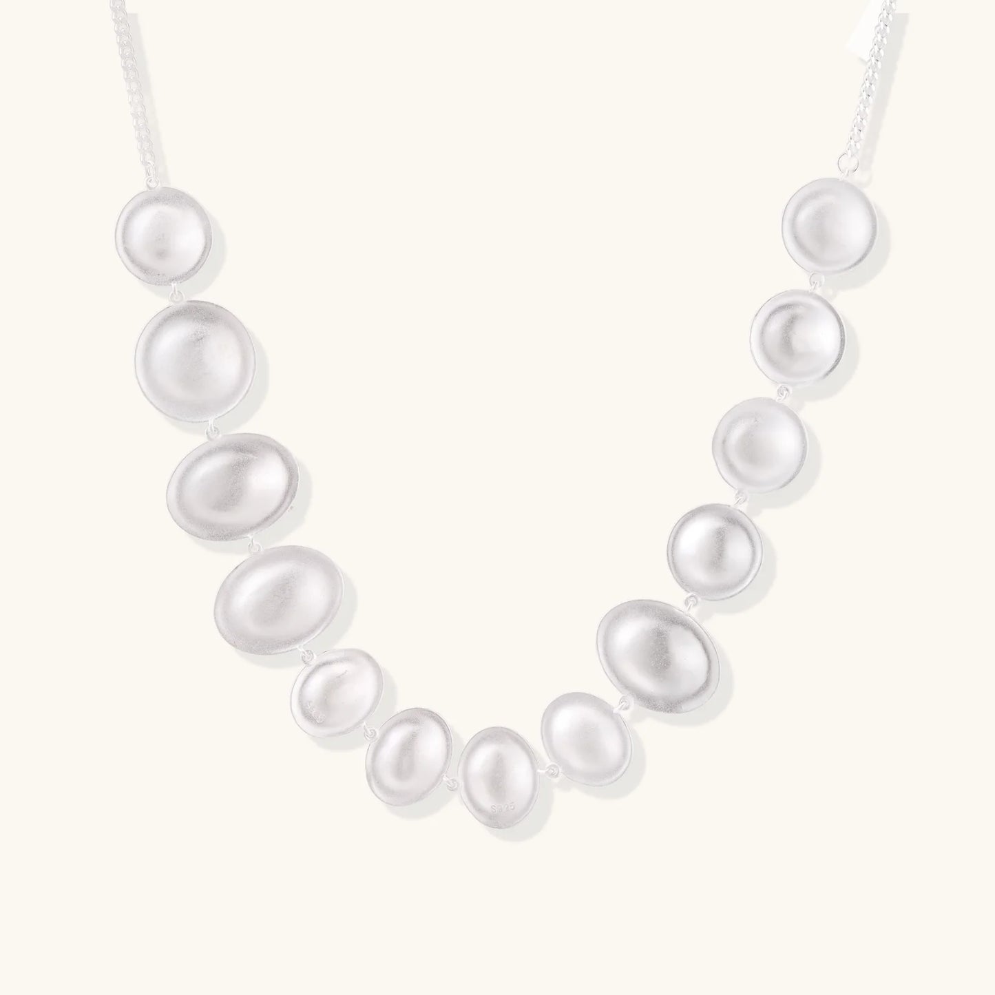 Graduated pearl-finish silver discs forming an organic bubble bib necklace on delicate chain against cream background.
