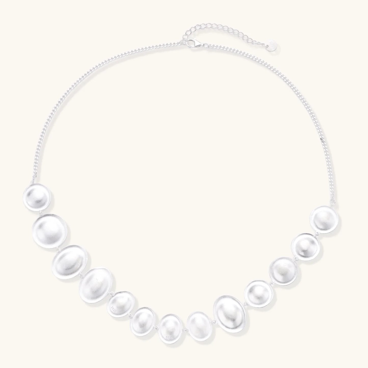 Graduated pearl-finish silver discs forming an organic bubble bib necklace on delicate chain against cream background.