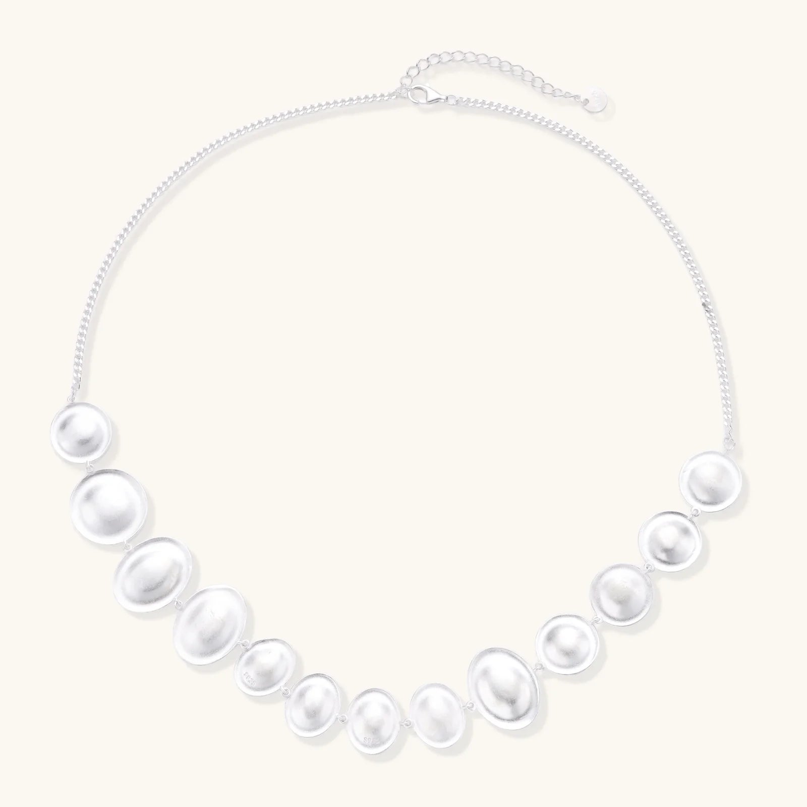 Graduated pearl-finish silver discs forming an organic bubble bib necklace on delicate chain against cream background.