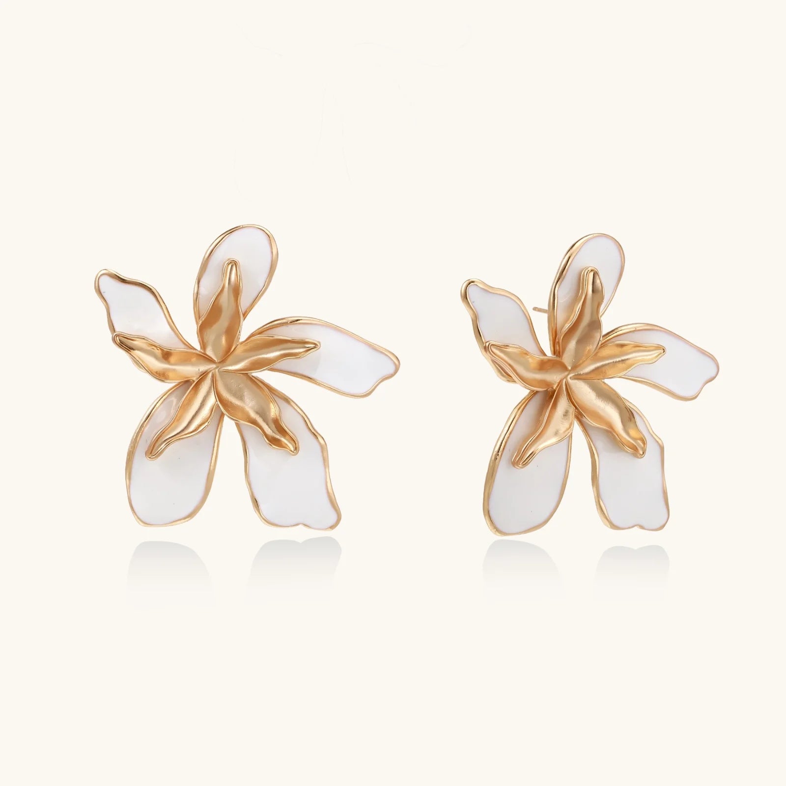 White enamel tropical flower earrings with sculptural gold-plated center and organic petal design on cream background