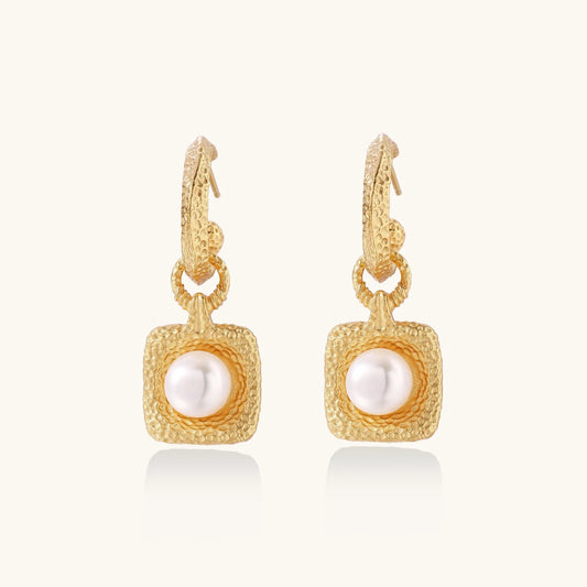 Pair of gold vermeil hoop earrings with textured square frames holding freshwater pearls on cream background