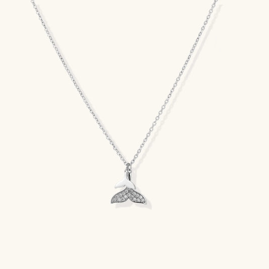 Delicate white gold plated whale tail pendant with pavé crystals on silver chain against cream background.